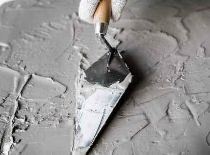 Hand of someone wearing gloves holding brick trowels from one of the best brick trowel brands spread plaster.